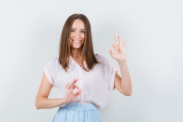 Jovem mulher mostrando sinal ok em t-shirt, saia e olhando alegre, vista frontal.