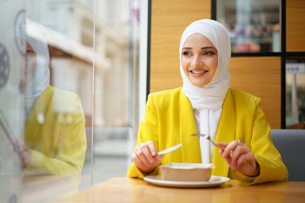 Jovem mulher muçulmana em hijab almoçando em um café