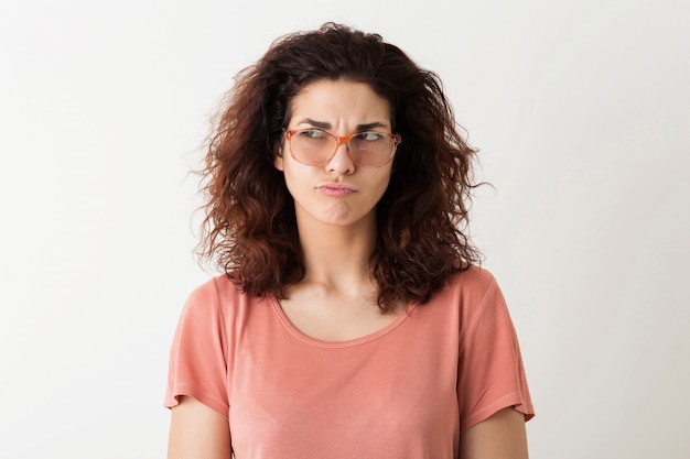 Jovem mulher muito elegante em óculos pensando, expressão do rosto pensativo, cabelos cacheados, tendo problema, emoção engraçada, isolado, camiseta rosa, estudante, franzindo a testa