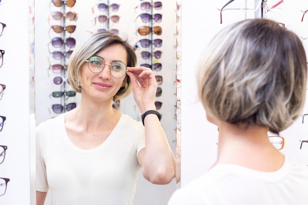 Jovem mulher na loja de ótica, escolhendo novos óculos com oculista. óculos na loja de ótica. uma mulher escolhe óculos. emoções. oftalmologia.