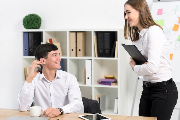 Jovem, mulher negócios fica, perto, a, sorrindo, homem negócios, falando telefone móvel