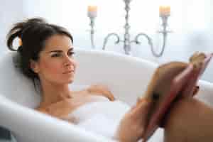 Foto grátis jovem mulher nua tomando um banho de espuma relaxante e lendo um livro