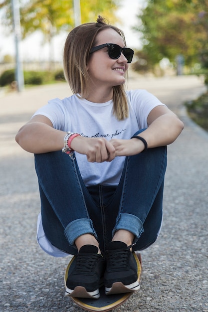 Jovem, mulher, óculos de sol, sentado, longboard