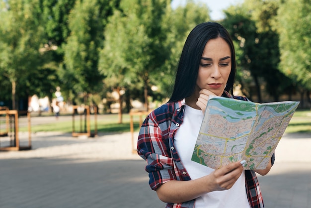 Jovem mulher olhando mapa e pensando no parque