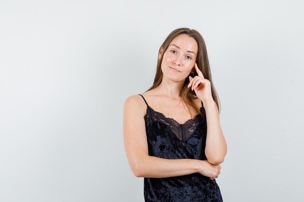 Jovem mulher olhando para a câmera enquanto pensa em uma camiseta preta e parece positiva