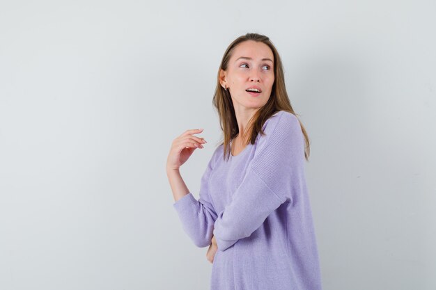 Jovem mulher olhando para trás com uma blusa lilás e parecendo sensata. vista frontal.