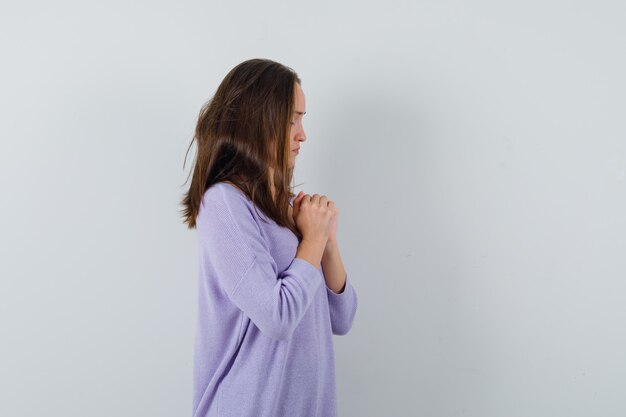 Jovem mulher orando com blusa lilás e parecendo calma.