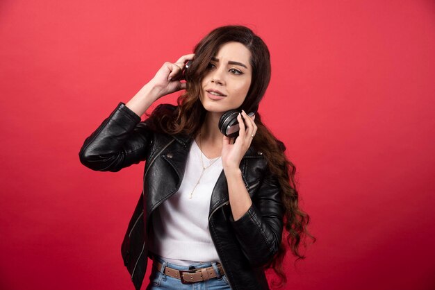 Jovem mulher ouvindo música em fones de ouvido e posando em um fundo vermelho. Foto de alta qualidade