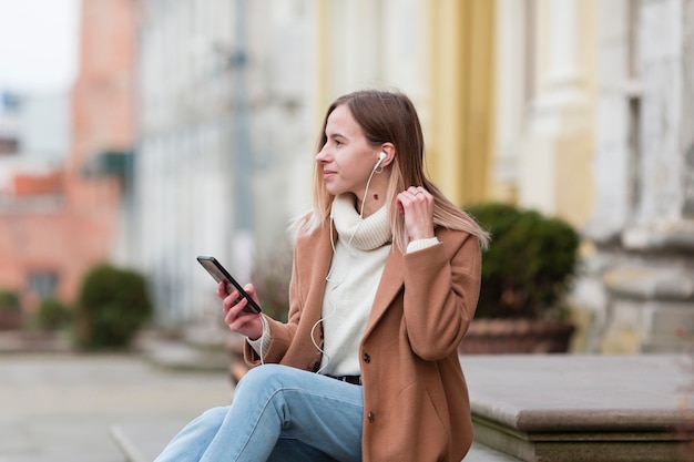 Jovem mulher ouvindo música em fones de ouvido na cidade