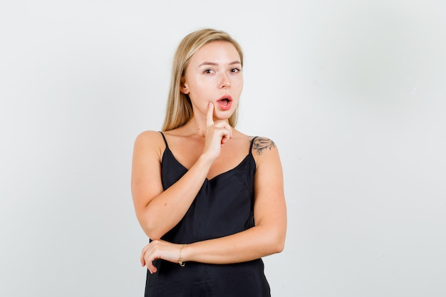 Jovem mulher pensando com o dedo perto da boca em uma camiseta preta