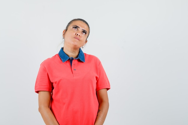 Jovem mulher pensando em algo em uma camiseta vermelha e parecendo pensativa. vista frontal.