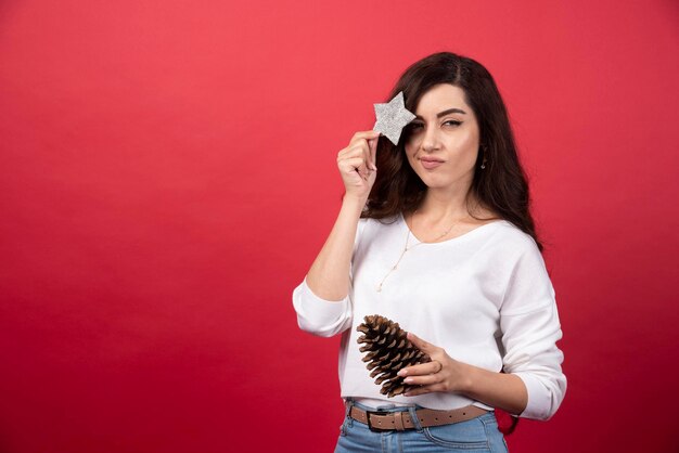 Jovem mulher posando com grande pinha de Natal e estrela sobre fundo vermelho. Foto de alta qualidade