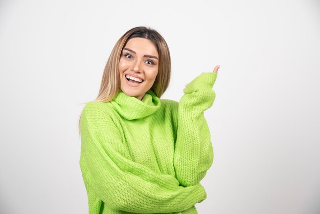 Jovem mulher posando com uma camiseta verde sobre uma parede branca.