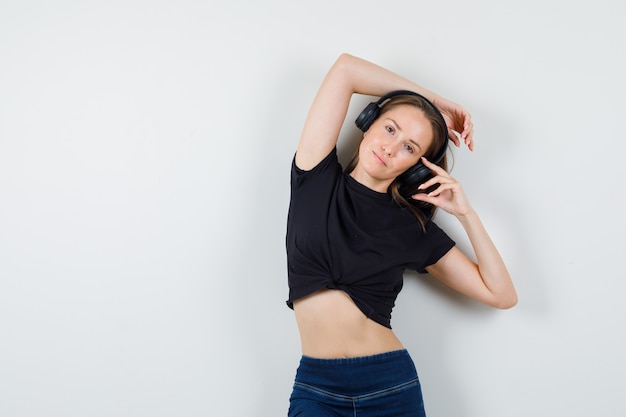 Jovem mulher posando enquanto toca fones de ouvido em uma blusa preta, calça e parecendo atraente