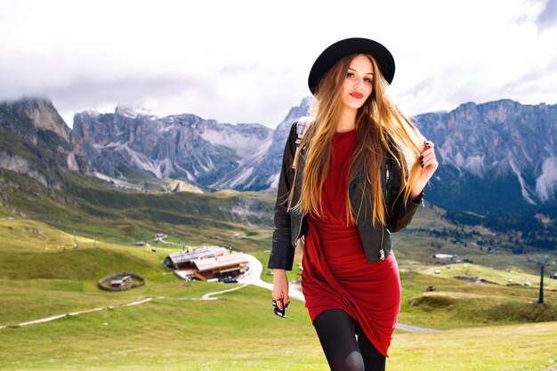 Jovem mulher posando nas montanhas Alp, usando vestido, jaqueta de couro, óculos escuros e mochila