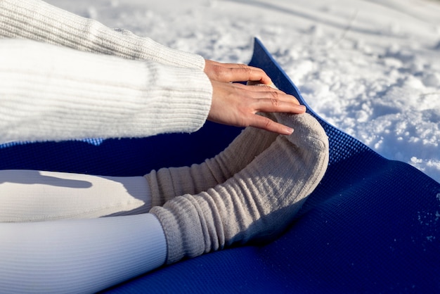 Jovem mulher praticando ioga ao ar livre durante o inverno em roupas quentes