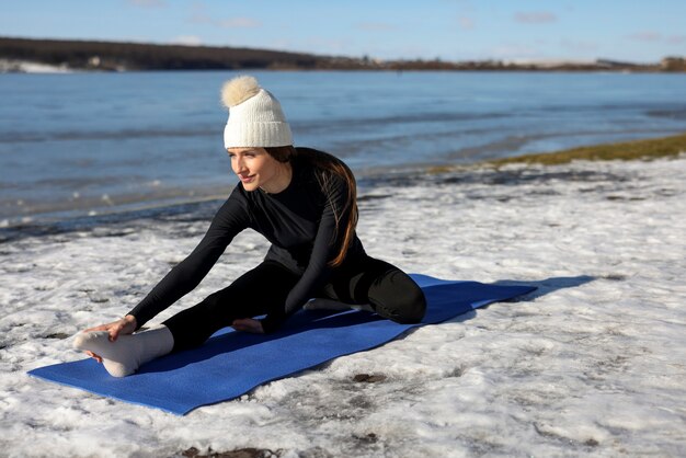 Jovem mulher praticando ioga ao ar livre durante o inverno na praia