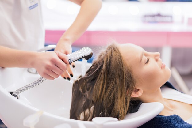Jovem mulher recebendo um novo penteado no salão de estilo de cabelo profissional. O cabeleireiro está massageando sua cabeça.