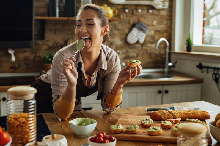 Foto grátis jovem mulher saboreando comida com os olhos fechados enquanto prepara bruschetta de abacate na cozinha