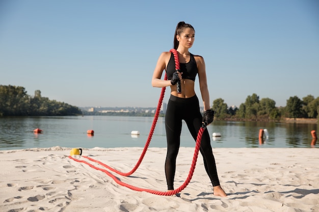 Jovem mulher saudável posando com cordas na praia.