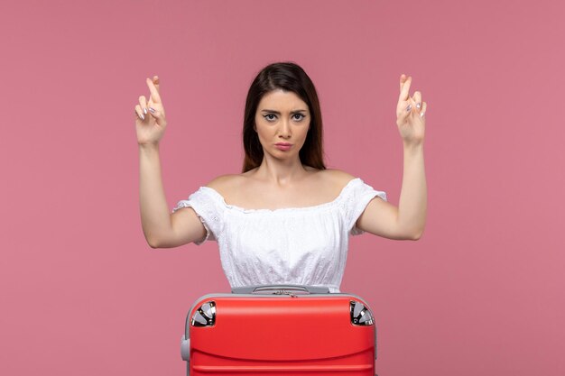 Jovem mulher se preparando para as férias com a bolsa, cruzando os dedos em uma viagem de fundo rosa no exterior