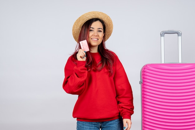 Jovem mulher se preparando para uma viagem e segurando o cartão do banco na parede branca.