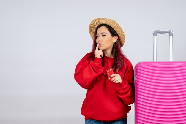 Jovem mulher se preparando para uma viagem e segurando o cartão do banco na parede branca.