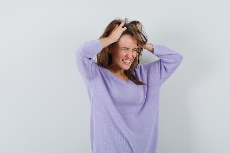 Foto grátis jovem mulher segurando a cabeça com as mãos em uma blusa lilás e parecendo estressante