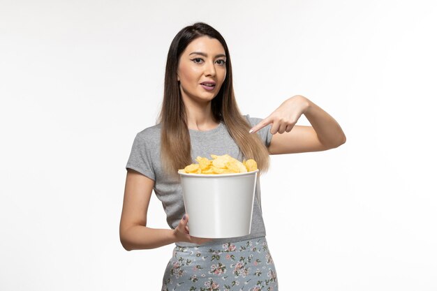 Foto grátis jovem mulher segurando a cesta com batata frita na superfície branca de frente