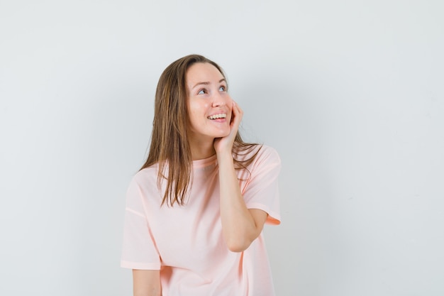 Jovem mulher segurando a mão na bochecha em t-shirt rosa e parece feliz.