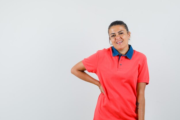 Jovem mulher segurando a mão na cintura em uma camiseta vermelha e bonita, vista frontal.