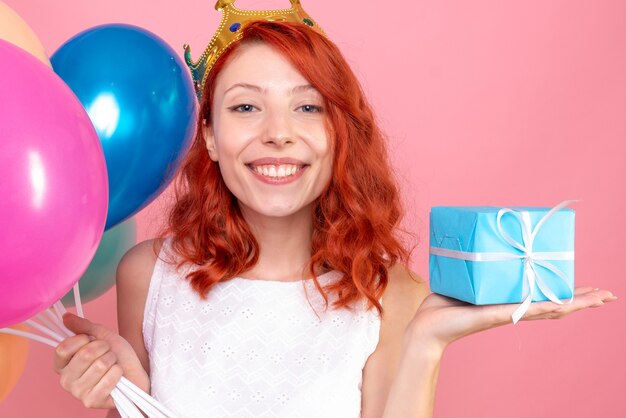 Jovem mulher segurando balões coloridos e presente na frente de perto