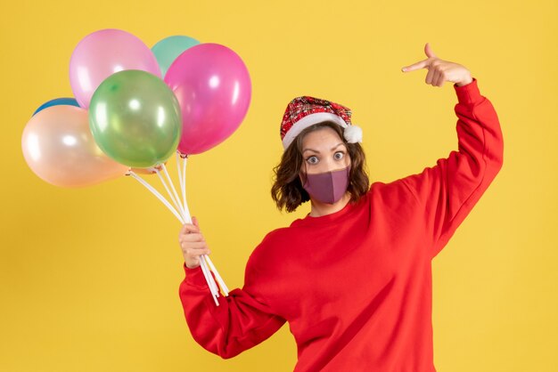 Jovem mulher segurando balões em máscara estéril em amarelo de frente