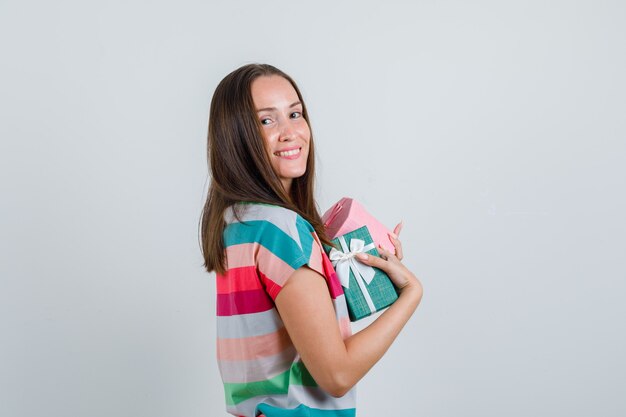 Jovem mulher segurando caixas de presentes em t-shirt e parecendo alegre.