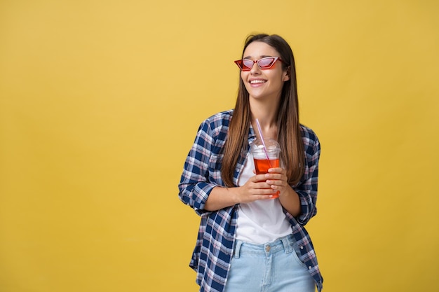 Foto grátis jovem mulher segurando e bebendo bebida gelada em roupas casuais menina bonita sorrindo feliz rindo olhando para a câmera