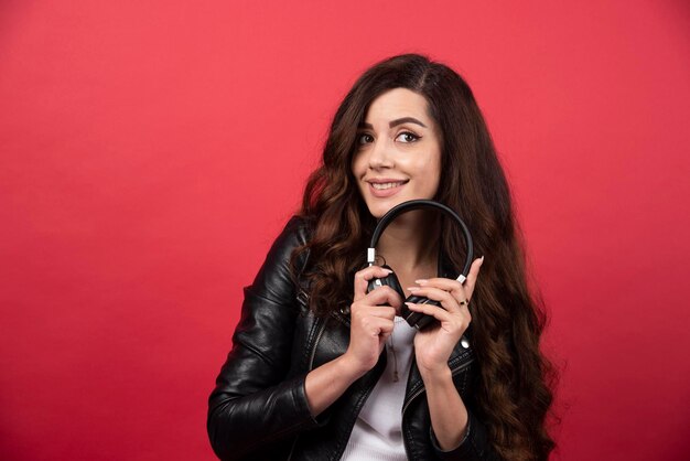 Jovem mulher segurando fones de ouvido e posando em um fundo vermelho. Foto de alta qualidade