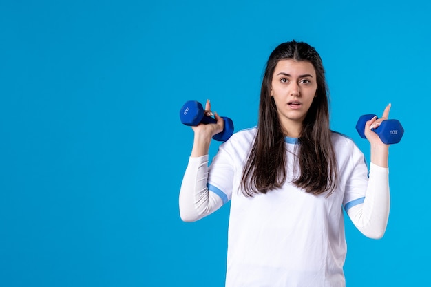 Jovem mulher segurando halteres azuis de frente