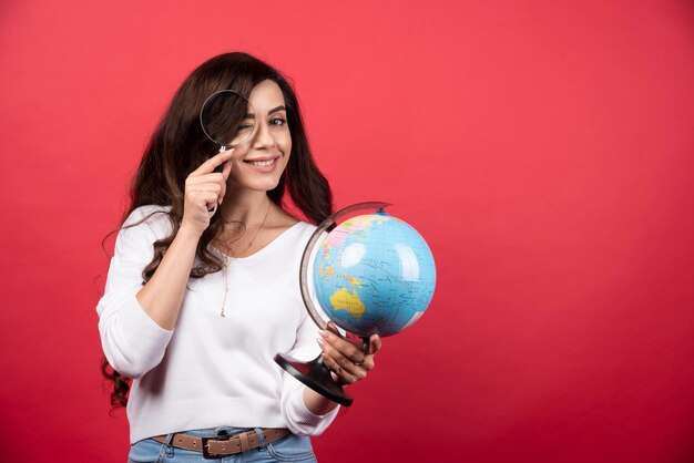 Jovem mulher segurando o globo e olhando com lupa. Foto de alta qualidade