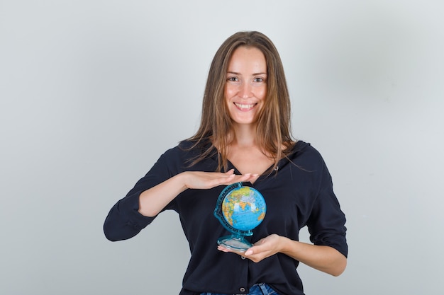 Jovem mulher segurando o globo em uma camisa preta, shorts jeans e parecendo feliz