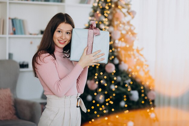 Jovem mulher segurando o presente de Natal pela árvore de Natal