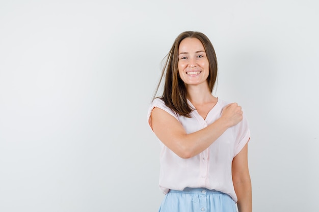 Foto grátis jovem mulher segurando o punho no peito em t-shirt, saia e parece confiante. vista frontal.