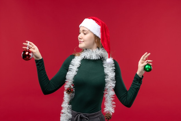 Jovem mulher segurando os brinquedos da árvore de natal no fundo vermelho.