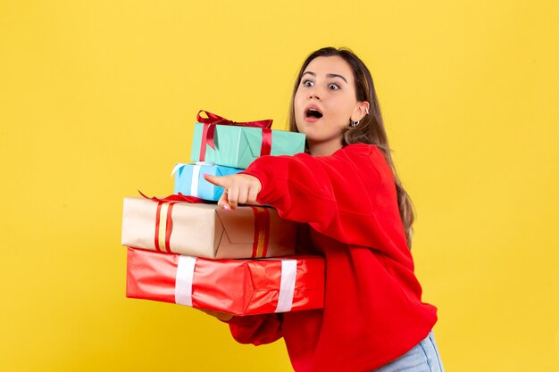 Jovem mulher segurando presentes de Natal em fundo amarelo