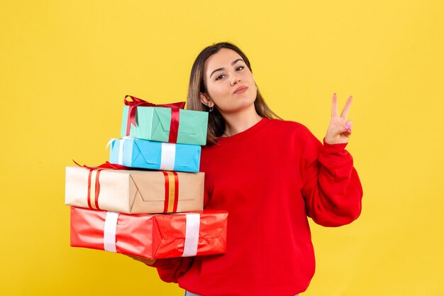 Jovem mulher segurando presentes de Natal em fundo amarelo