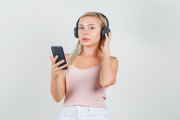 Jovem mulher segurando smartphone em camiseta, minissaia, fones de ouvido