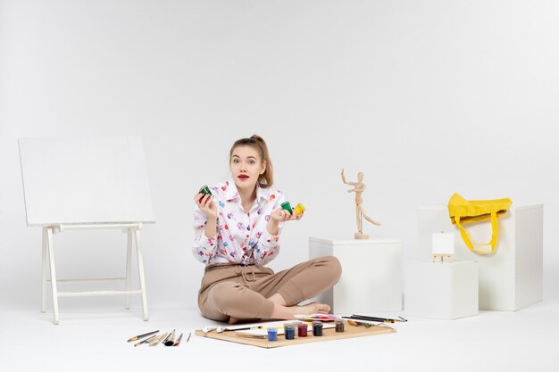 Jovem mulher segurando tintas coloridas dentro de latas em fundo branco.