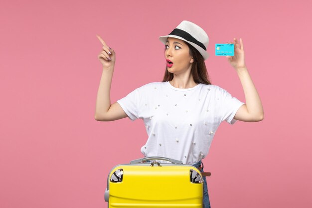 Jovem mulher segurando um cartão azul do banco na cor da parede rosa claro de frente