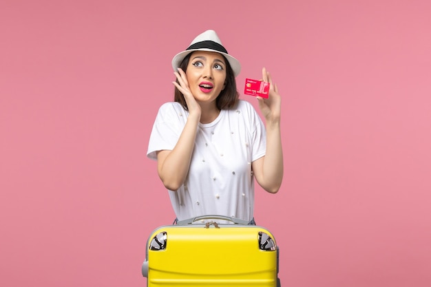 Jovem mulher segurando um cartão de banco vermelho na parede rosa viagem colorida verão