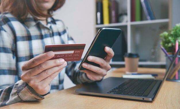 Jovem mulher segurando um cartão de crédito e usando telefone inteligente, comprando onl