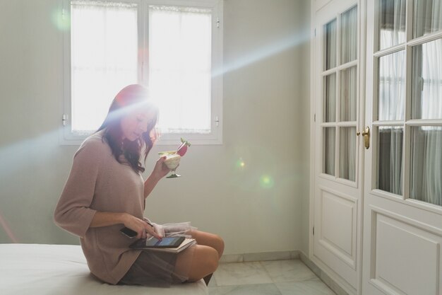 Jovem mulher segurando um cocktail e usando seu tablet